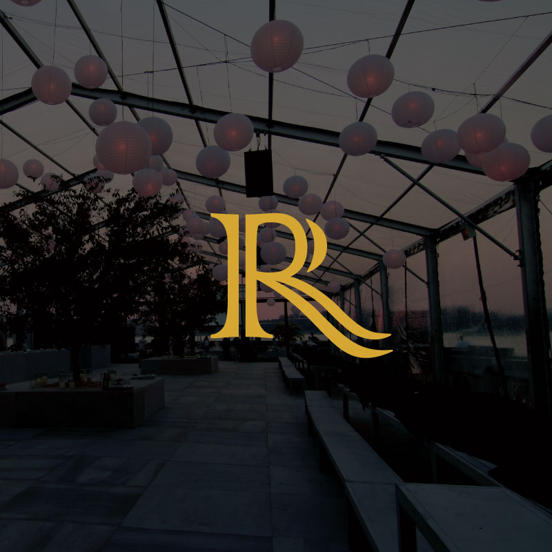 A large gold R logo is centred over a dimly lit, open air venue with hanging white lanterns and transparent walls, overlooking trees and a cityscape at dusk