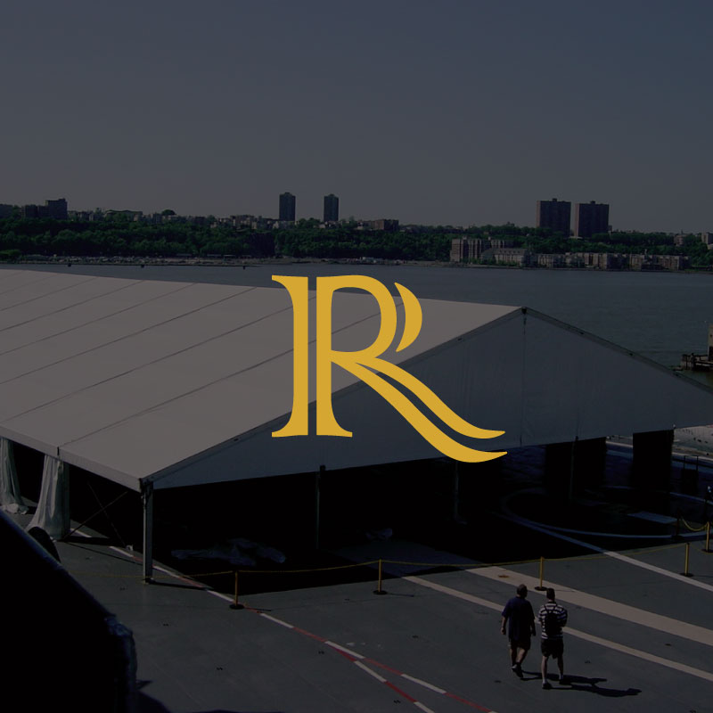 A large white event marquee is set up near a waterfront with trees and buildings in the background Two people walk beside the marquee A stylised gold R logo is overlaid in the centre of the image
